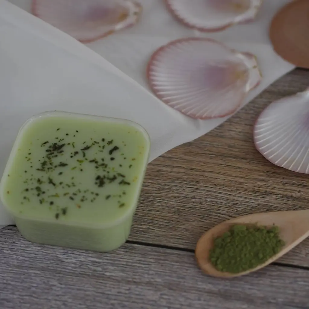 Pale green dessert and a wooden spoon of matcha powder among pink shells