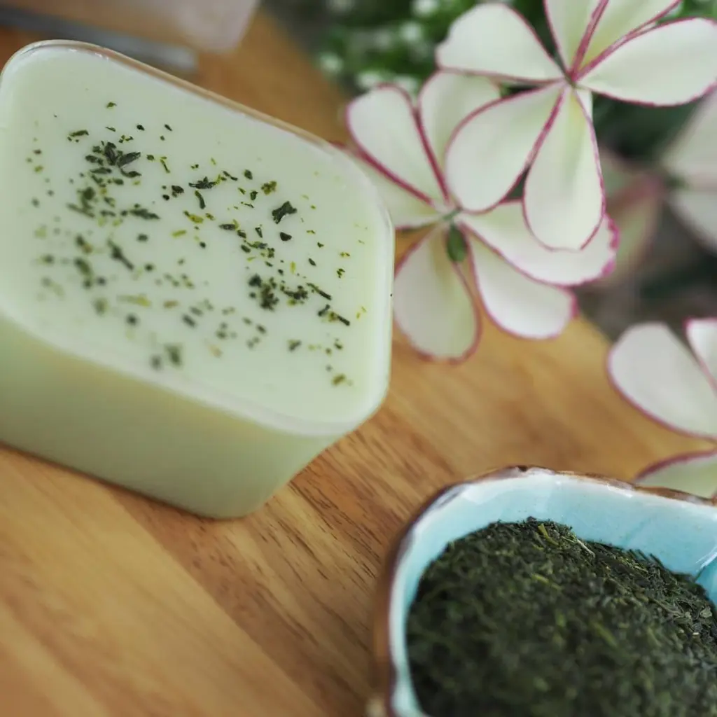 Pale green dessert with tea leaves beside white flowers and a bowl of loose tea