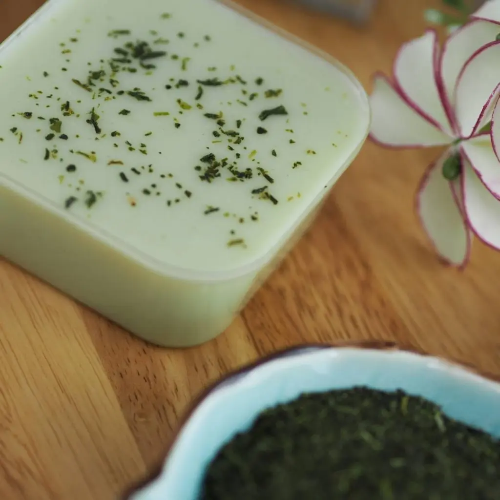 Square container of pale green pudding topped with tea flakes