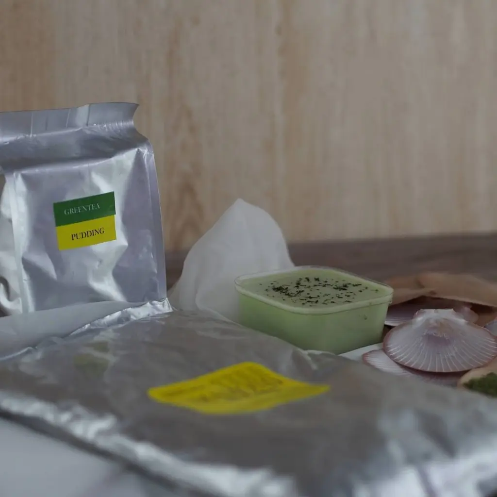 Green tea pudding surrounded by silver pouches and decorative shells