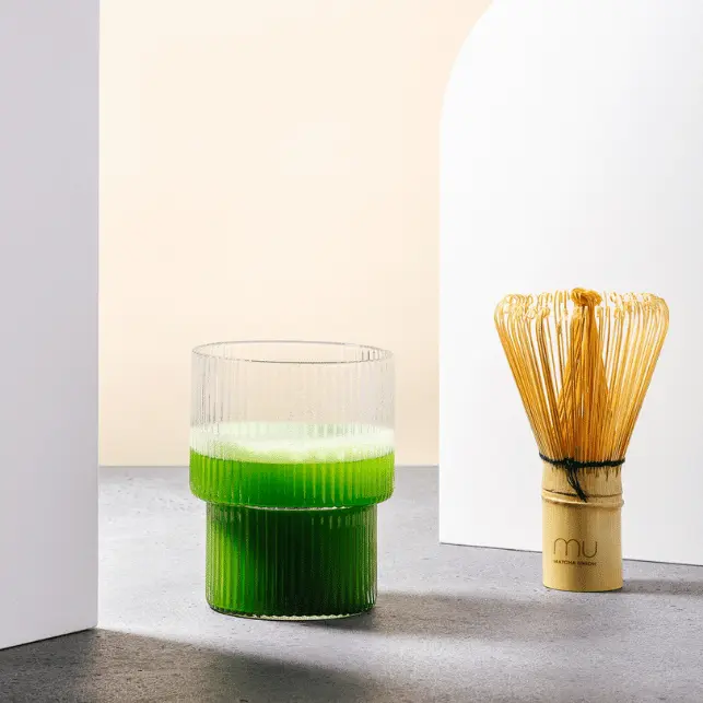 Bamboo matcha whisk beside a ribbed glass of bright green matcha