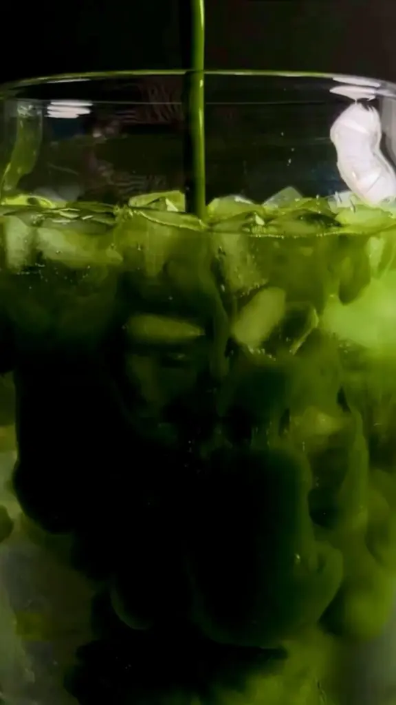 Dark green matcha pouring over ice cubes in a clear glass