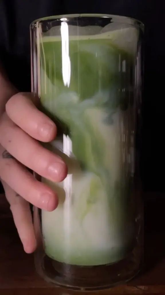 Hand holding a tall glass of marbled green and white iced matcha