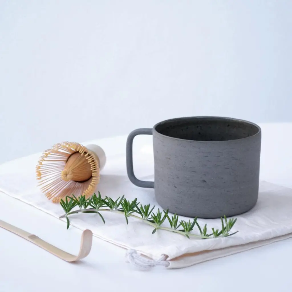 Gray mug, bamboo whisk, bamboo spoon, and rosemary on folded white fabric