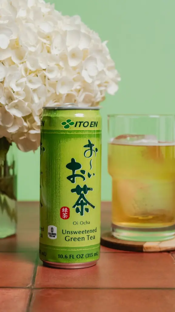 ITO EN green tea can beside a glass of amber tea and white flowers
