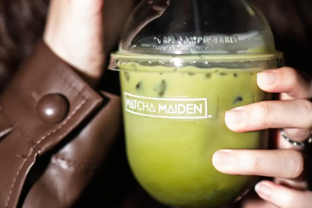 Hand holding a light green iced drink in a Matcha Maiden cup