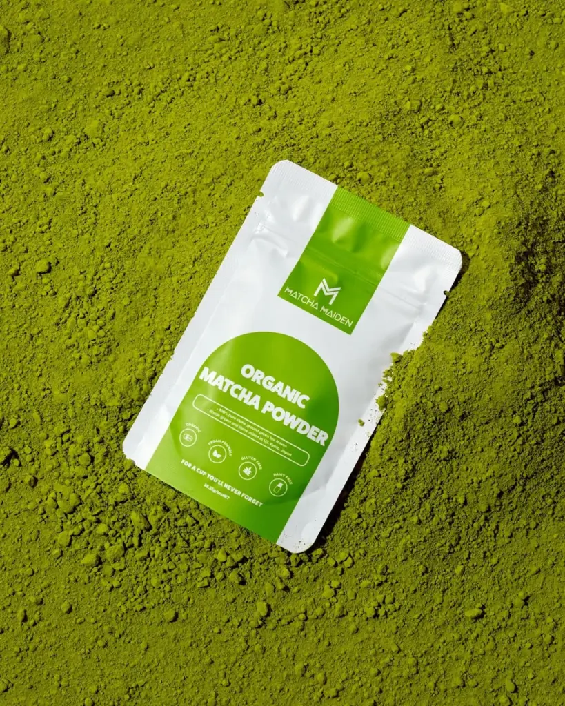 White and green Matcha Maiden pouch resting on bright green matcha powder