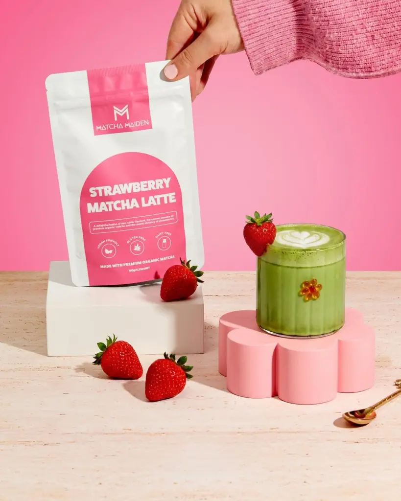 Strawberry Matcha Latte pouch beside a green latte and fresh strawberries