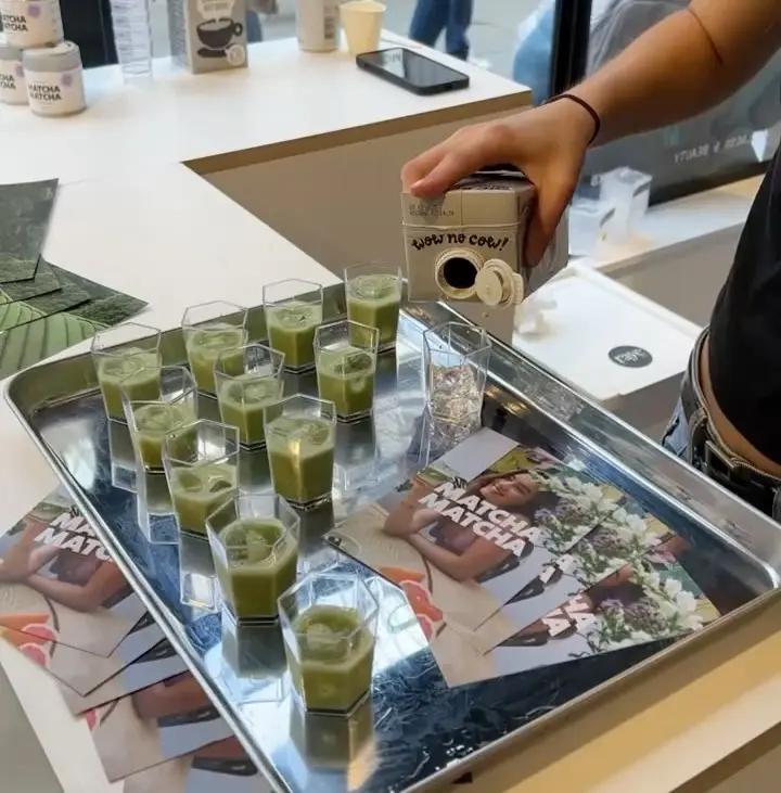 Small glasses of green drink on a metal tray as liquid is poured from a carton