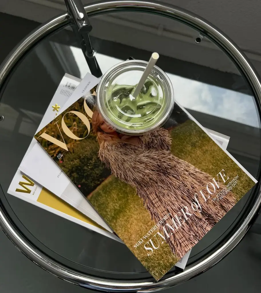 Iced green drink with a straw resting on magazines atop a round glass table