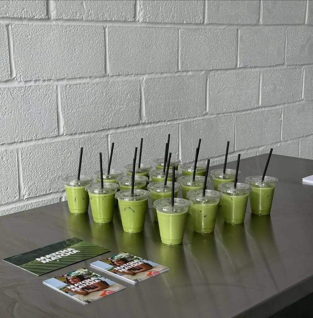 Rows of iced green drinks with black straws on a metal table