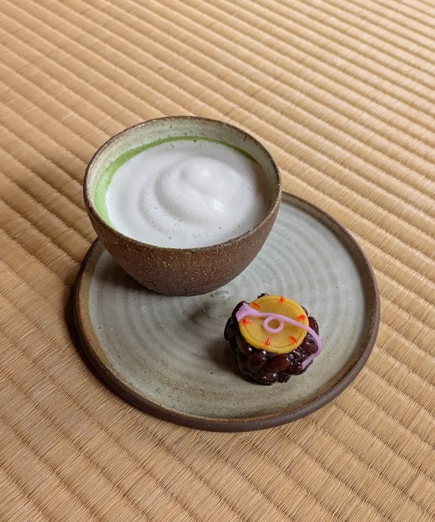 Ceramic cup of frothy matcha beside a colorful decorated sweet on a plate