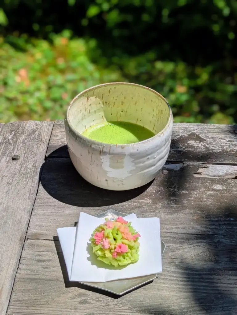 Ceramic bowl of bright green matcha with a pink and green floral sweet