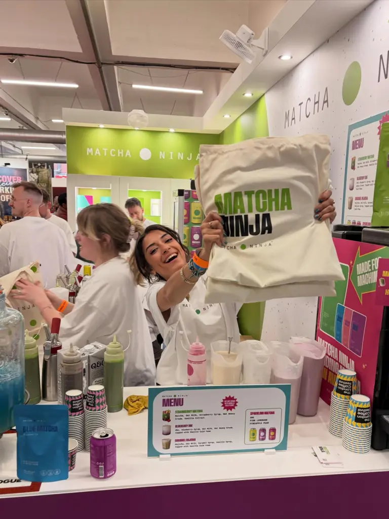 Smiling staff member holding up a Matcha Ninja tote behind a colorful drink counter