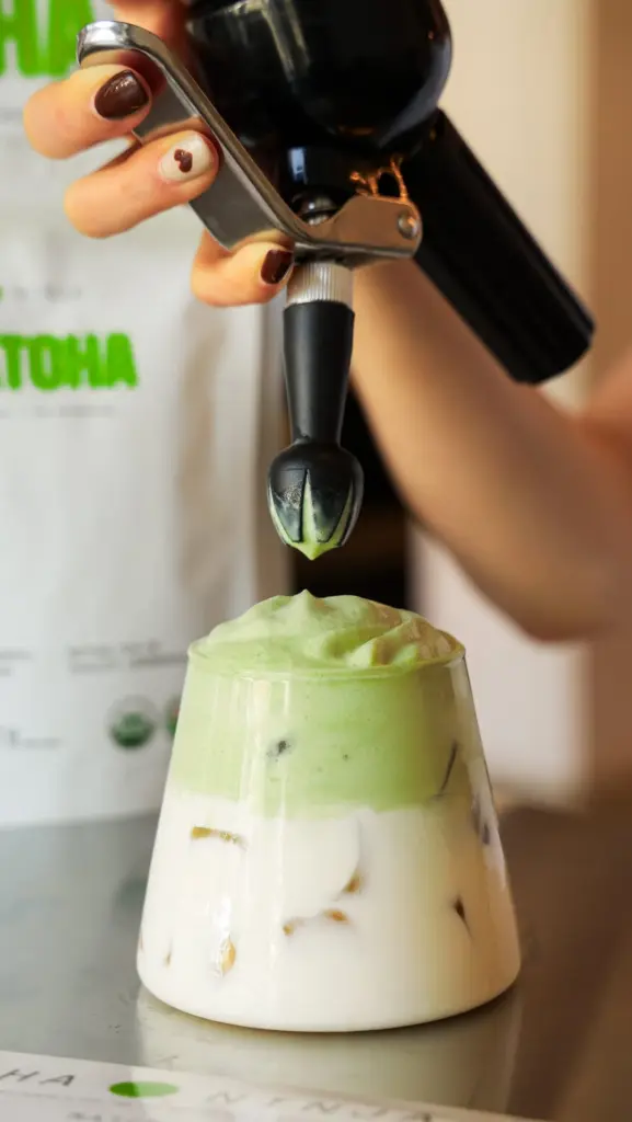 Green foam being dispensed onto a layered iced latte