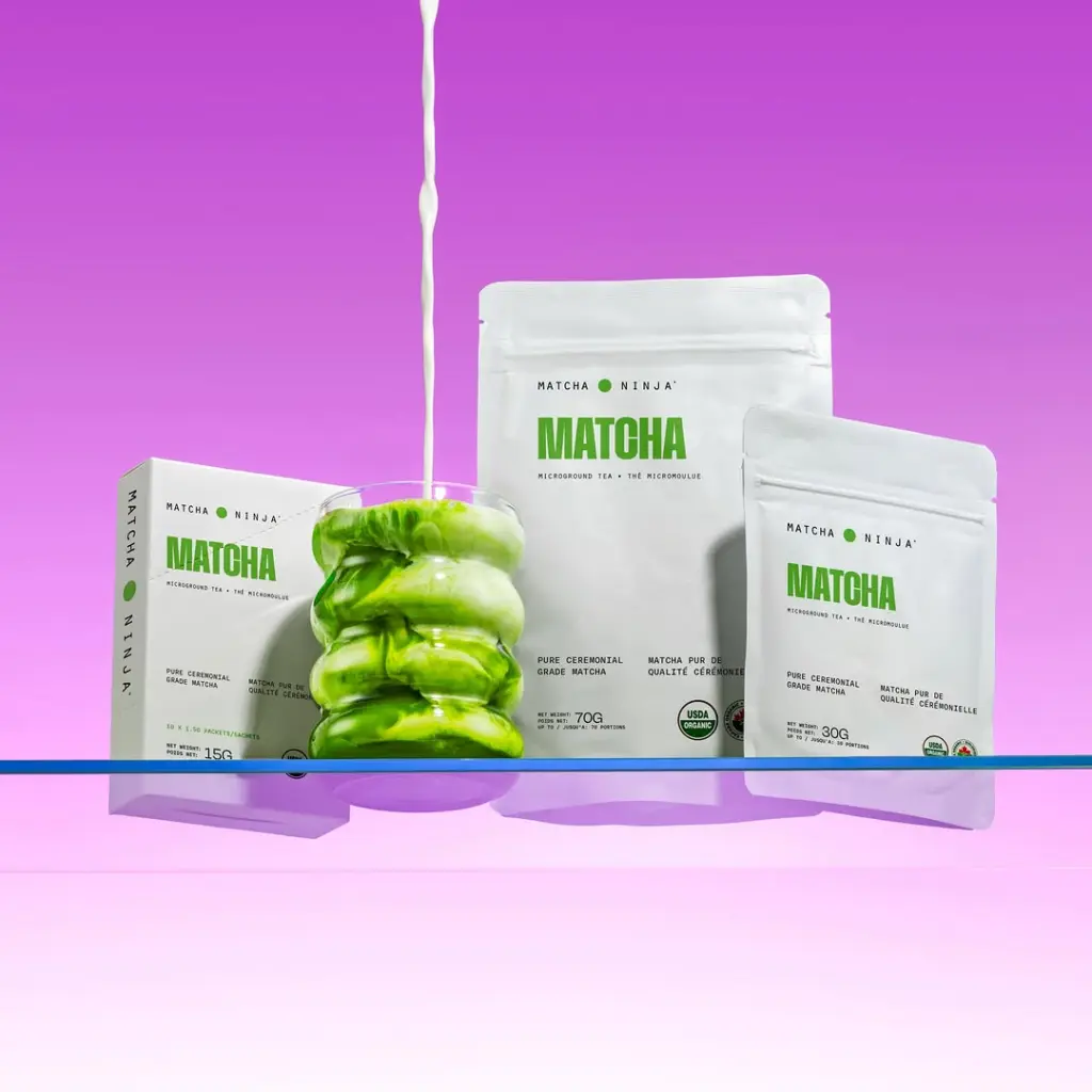 Three white Matcha packages beside a green marbled iced drink as white liquid pours in