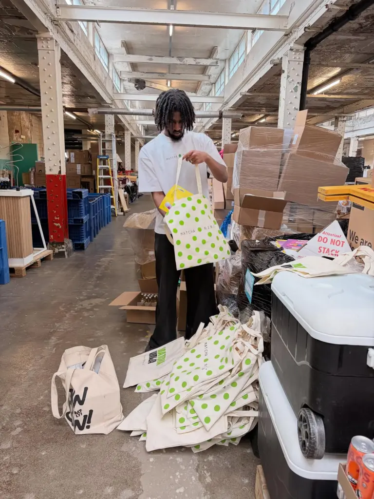Person holding a green polka-dot Matcha Ninja tote beside a pile of bags