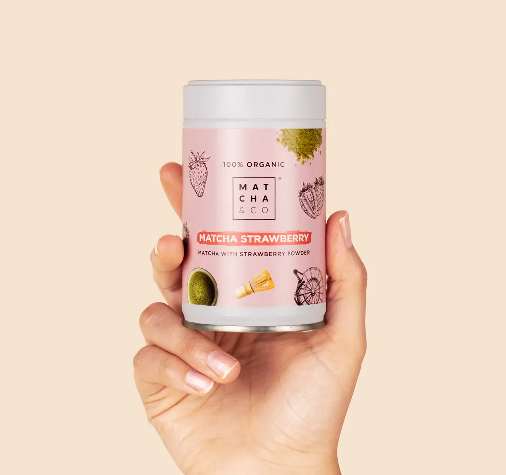 Hand holding a pink Matcha & CO Matcha Strawberry tin against a pale beige background