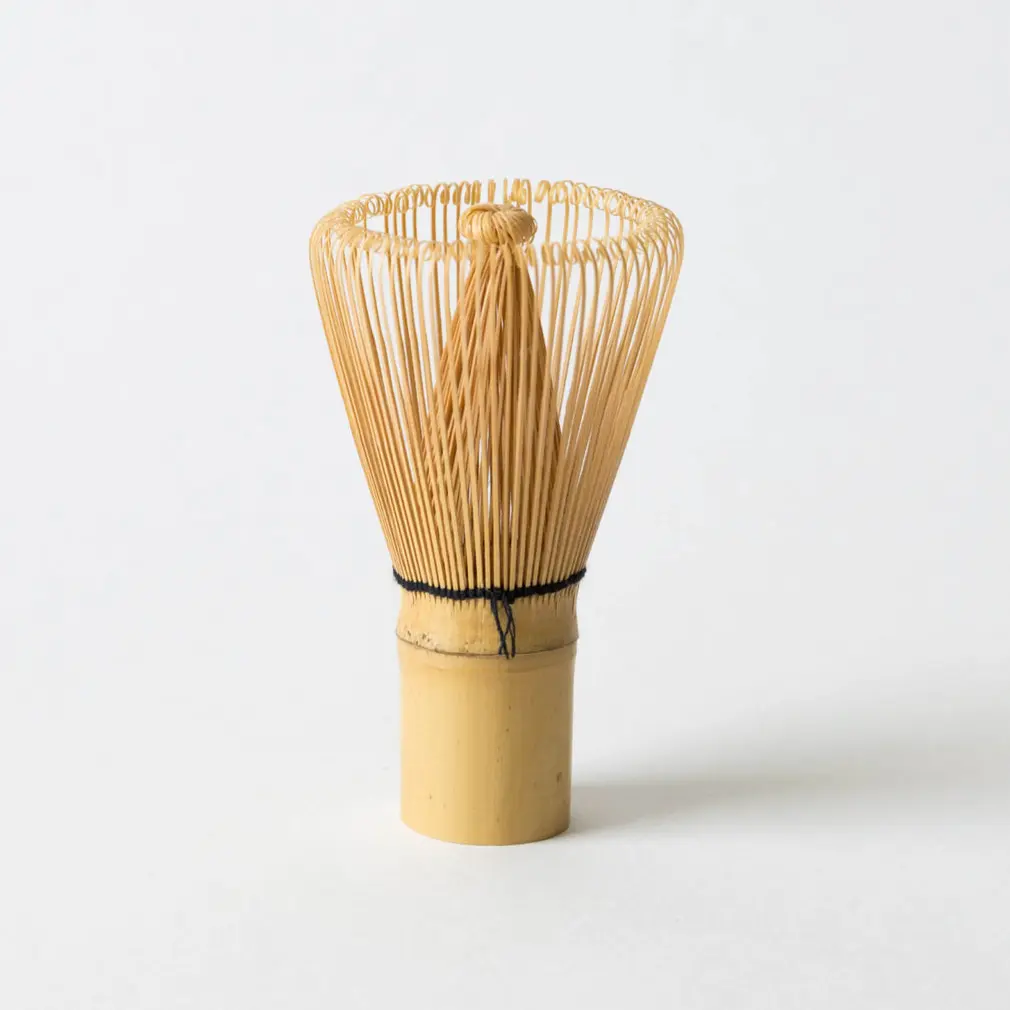 Bamboo matcha whisk standing upright against a plain white background