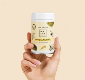 Hand holding a Matcha & CO Matcha Vanilla container against a pale beige background