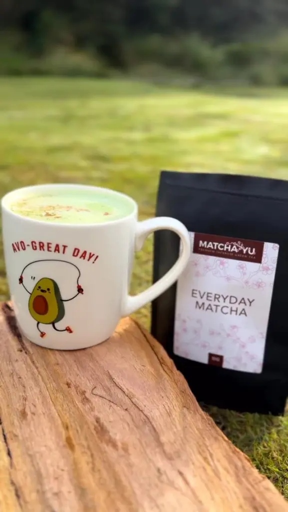 Green drink in a white avocado mug beside a black Everyday Matcha pouch