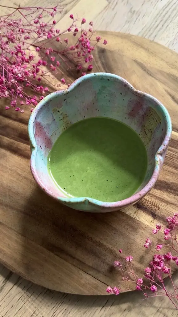Green matcha in a pastel flower-shaped bowl with pink dried flowers