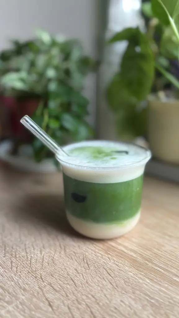 Layered green and white iced matcha drink with foam and a glass straw
