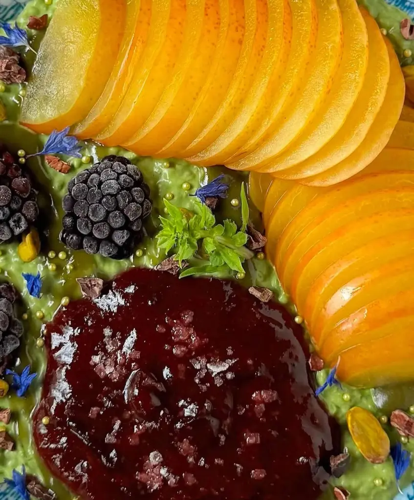 Close-up of sliced orange fruit, frozen blackberries, and red compote on a green base