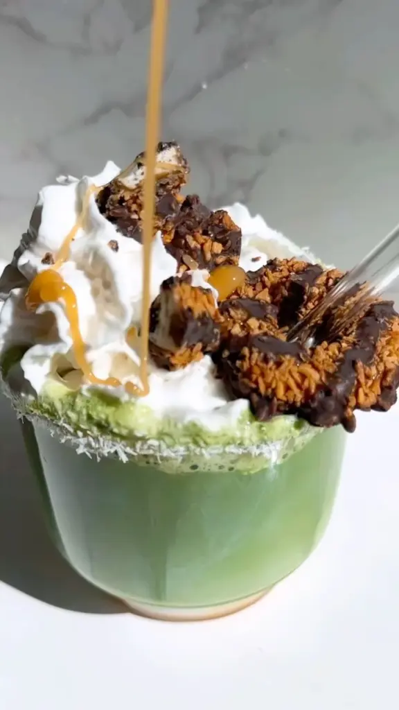 Green drink topped with whipped cream, chocolate-coated clusters, and golden sauce