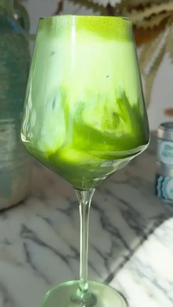 Bright green iced matcha swirling with milk in a stemmed glass