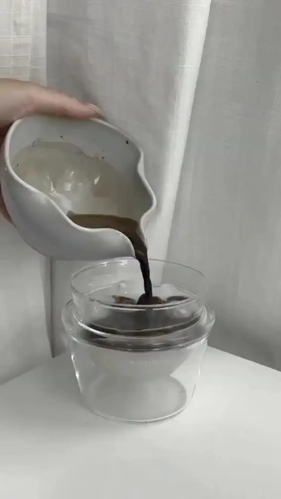 Dark liquid pouring from a white pitcher into a glass of ice