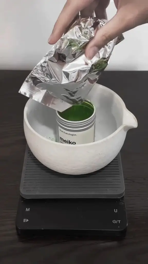 Hand lifting a silver pouch from an open Meiko tin inside a white bowl