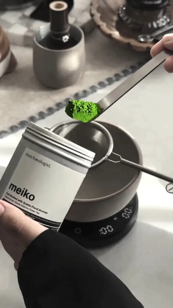 Scoop of vivid green powder held above a fine-mesh sifter and bowl