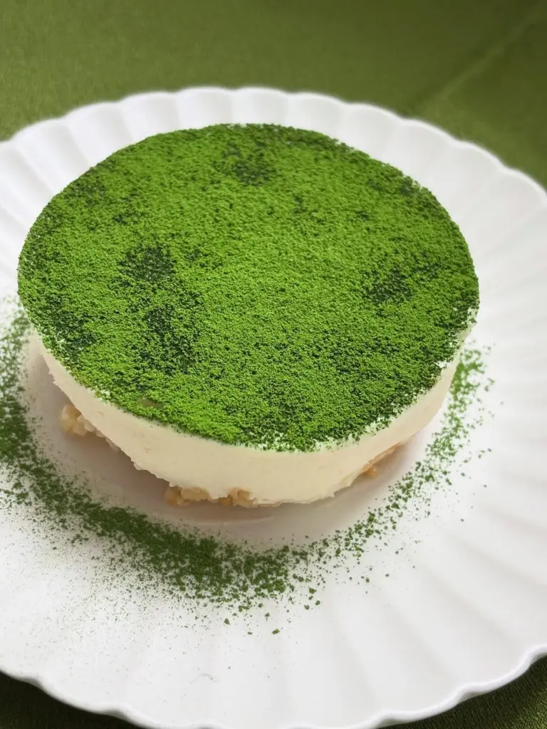Round white dessert covered with green powder on a scalloped plate