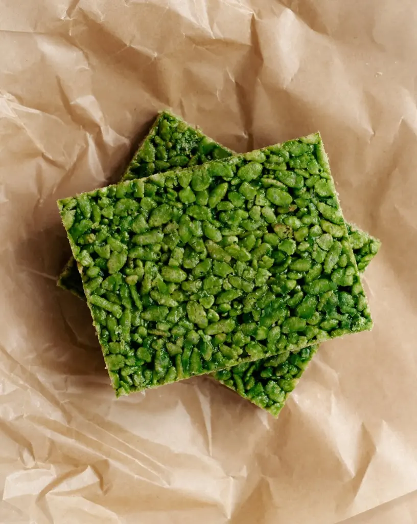 Three green puffed-grain snack squares stacked on brown paper