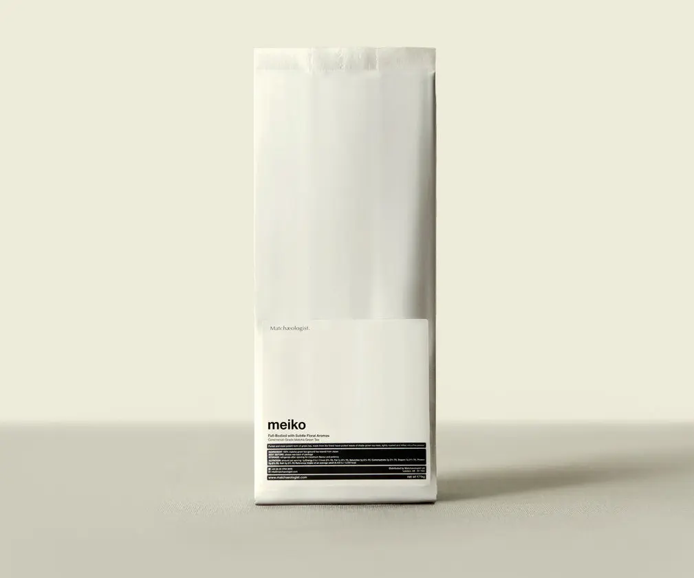 Tall white Matchæologist Meiko matcha package with a small black-and-white front label