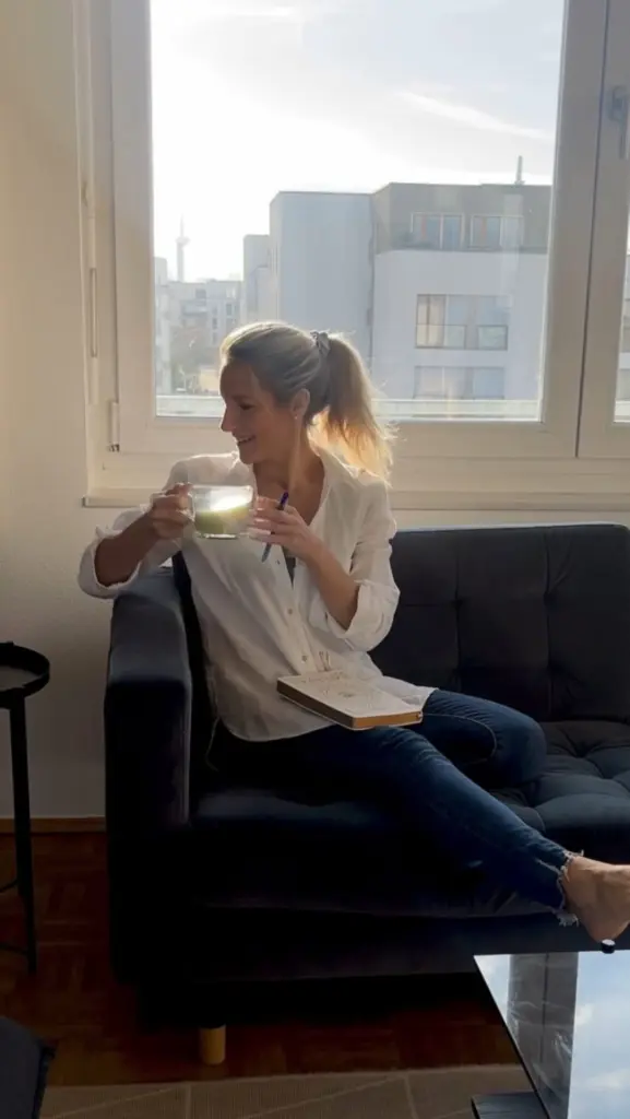 Smiling woman seated on a sofa holding a glass mug of green drink