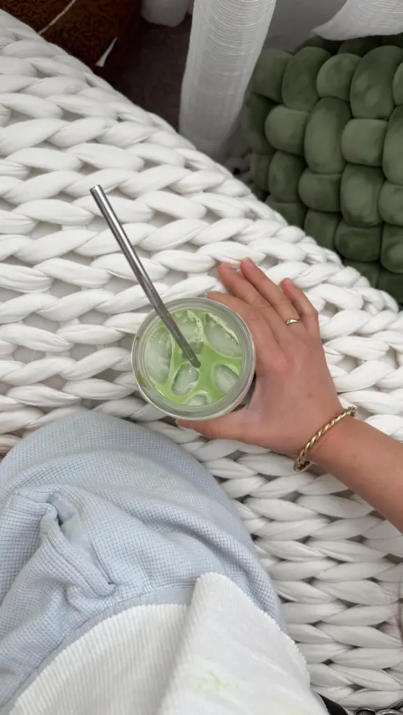 Iced green drink with a metal straw resting on a chunky white knit blanket