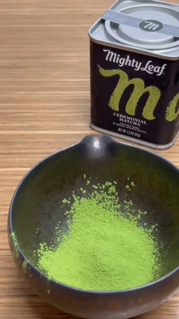 Bright green matcha powder in a dark bowl beside a Mighty Leaf tin