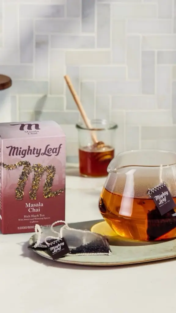 Mighty Leaf Masala Chai box beside a glass teapot and tea pouches