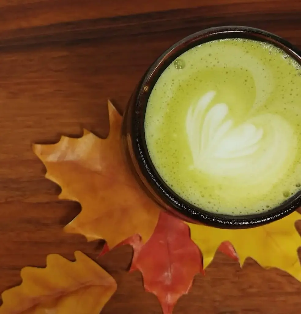 Green matcha latte with leaf-shaped foam art among colorful autumn leaves