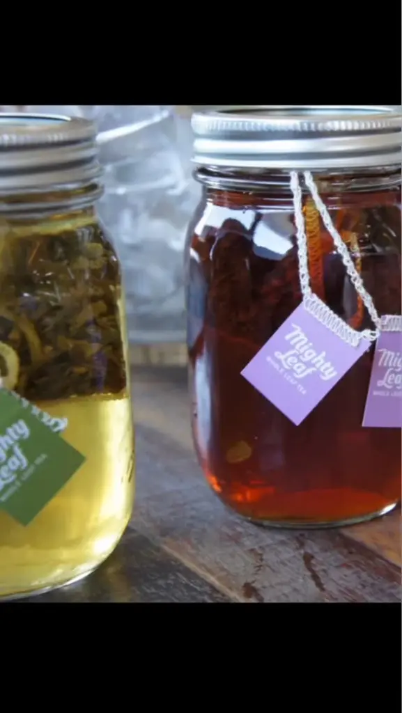 Amber and pale green teas steeping in lidded glass jars with Mighty Leaf tags