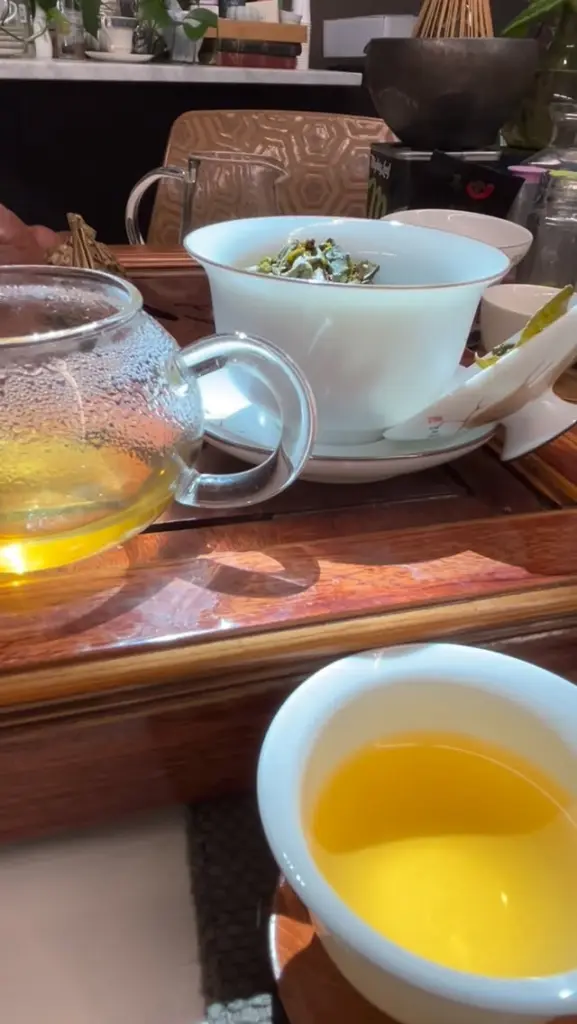 Golden tea in a white cup beside a glass teapot and loose leaves