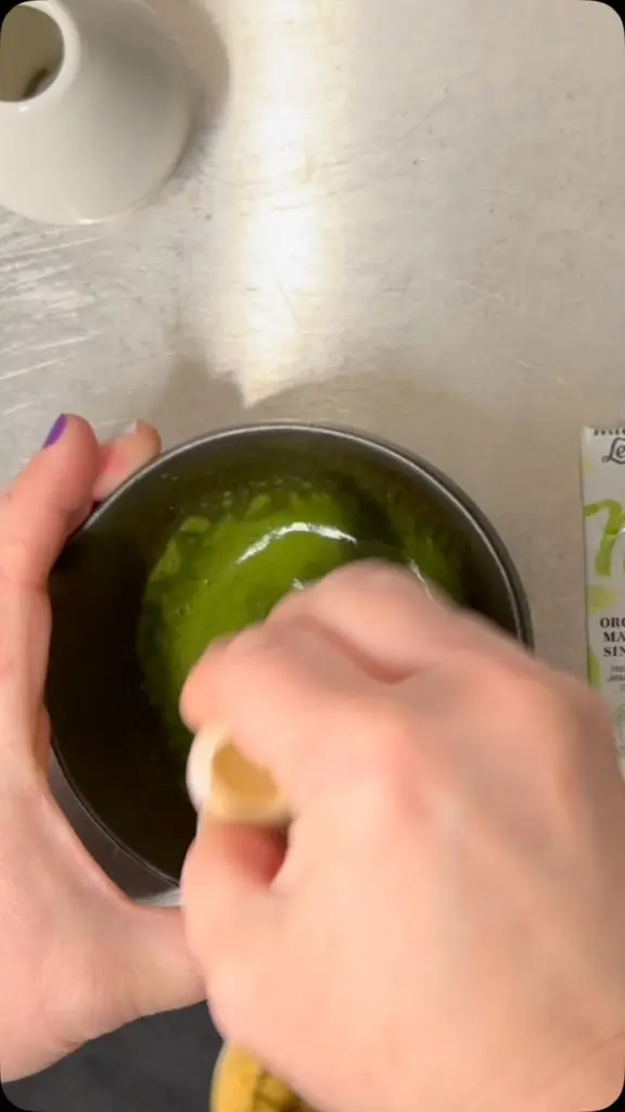 Hands whisking bright green matcha in a dark bowl