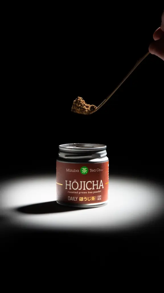 Spoonful of brown tea powder held above an open Mizuba Hōjicha tin