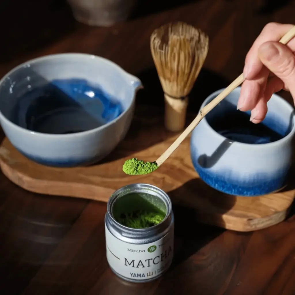 Hand holding a bamboo scoop of green matcha powder above an open tin