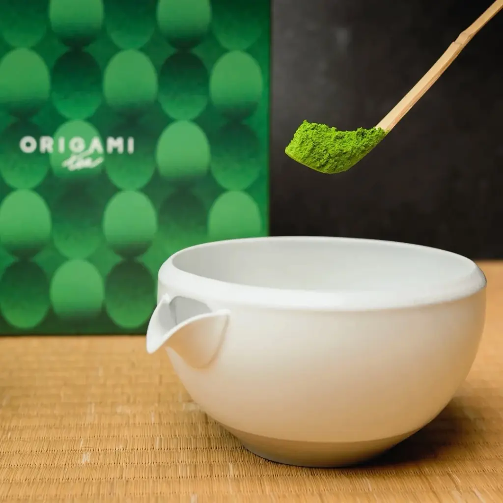 Bamboo scoop holding bright green matcha powder above a white bowl