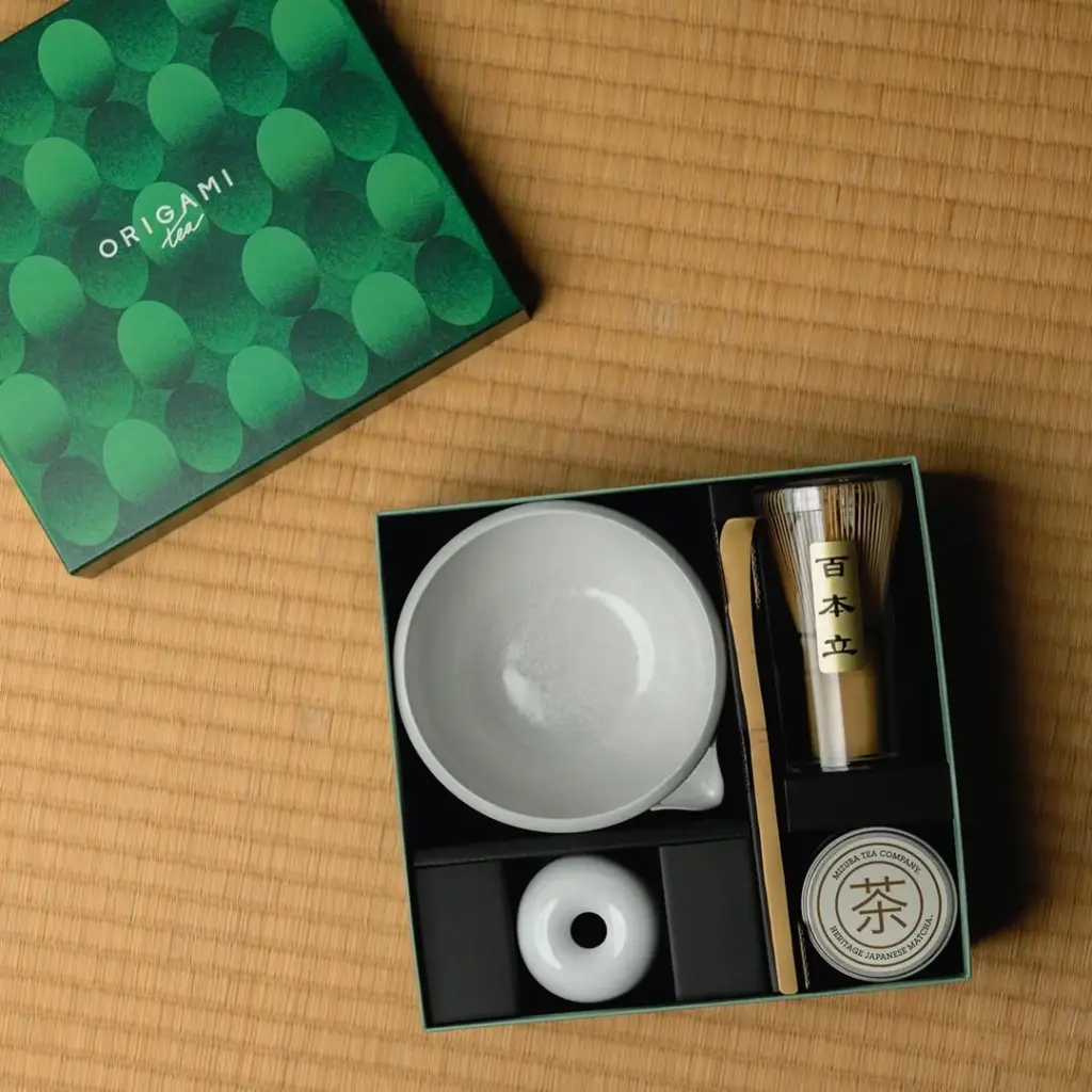 Open matcha set with white bowl, bamboo whisk, scoop, whisk stand, and Mizuba tin