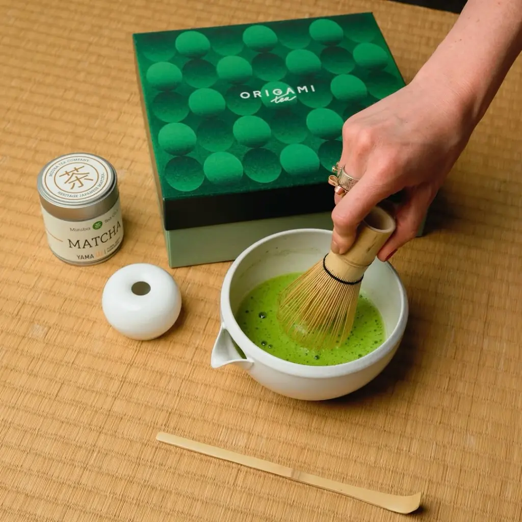 Hand whisking bright green matcha in a white spouted bowl
