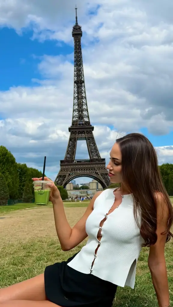 Woman holding a clear cup of green matcha with the Eiffel Tower behind her